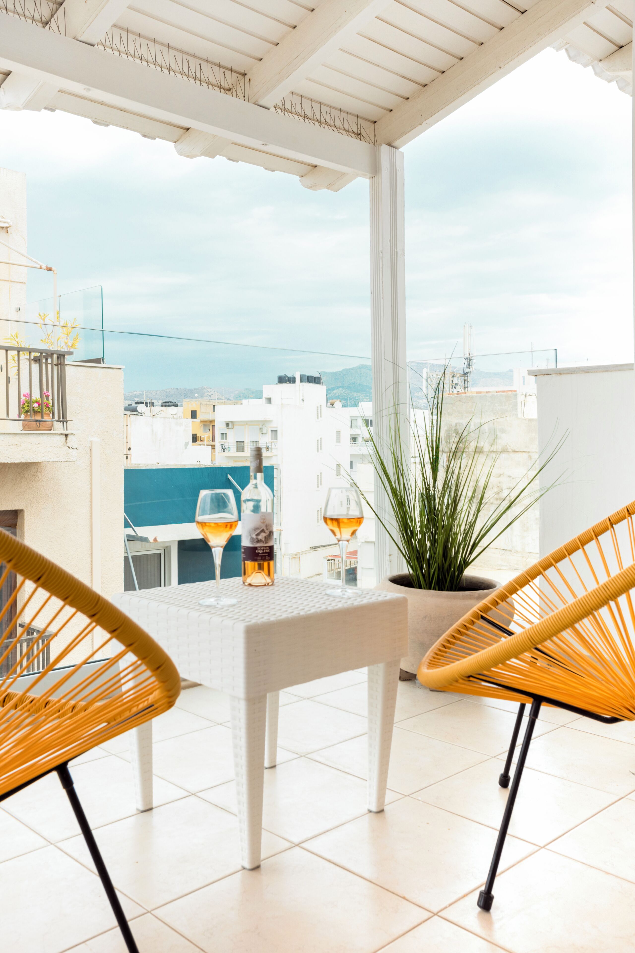 A balcony with wicker chairs, a table, and a bottle of wine.