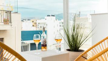 A balcony with wicker chairs, a table, and a bottle of wine.