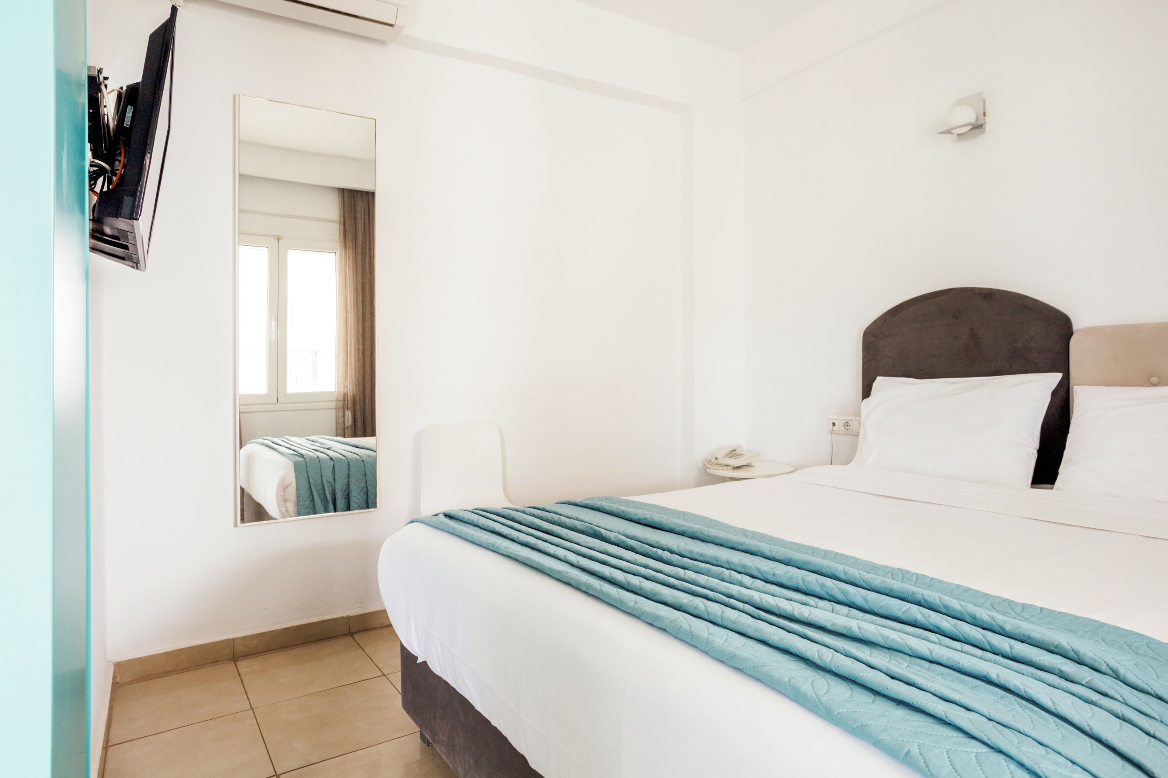 Ein Hotelzimmer mit einem Bett, einem Nachttisch, einem Spiegel und einem Fenster.