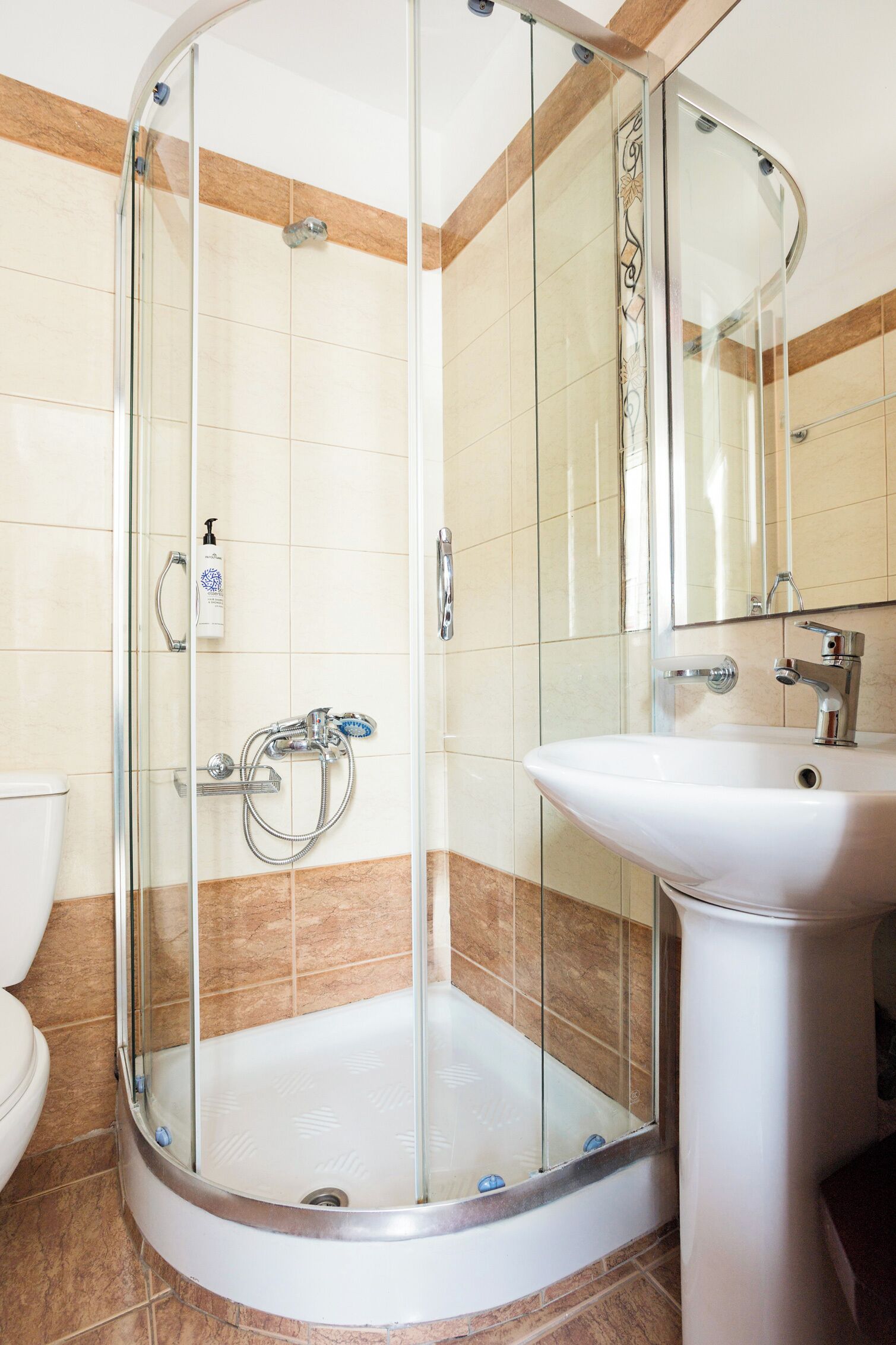 Un baño con ducha envuelta en vidrio, un lavamanos blanco y un espejo sobre él.