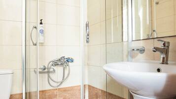 Un baño con ducha envuelta en vidrio, un lavamanos blanco y un espejo sobre él.