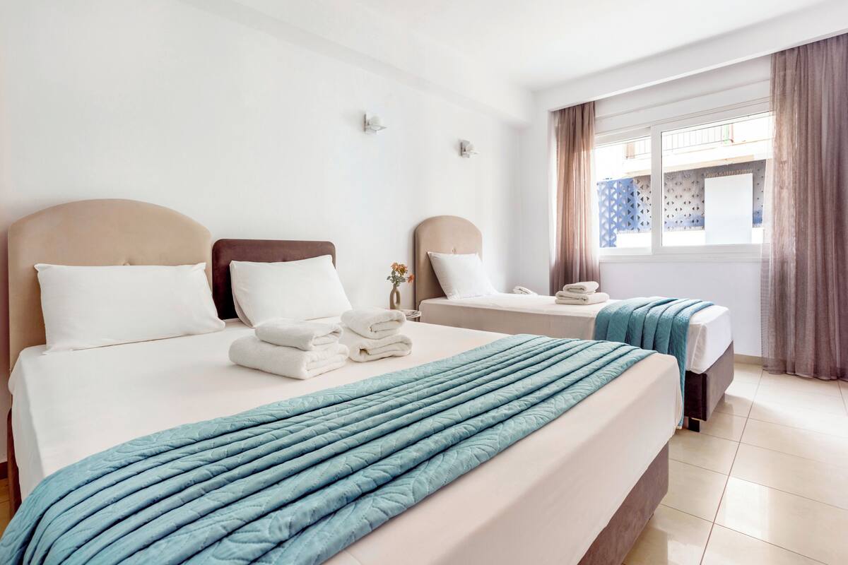 A hotel room with two beds, a large window with curtains, and a view of the outside.