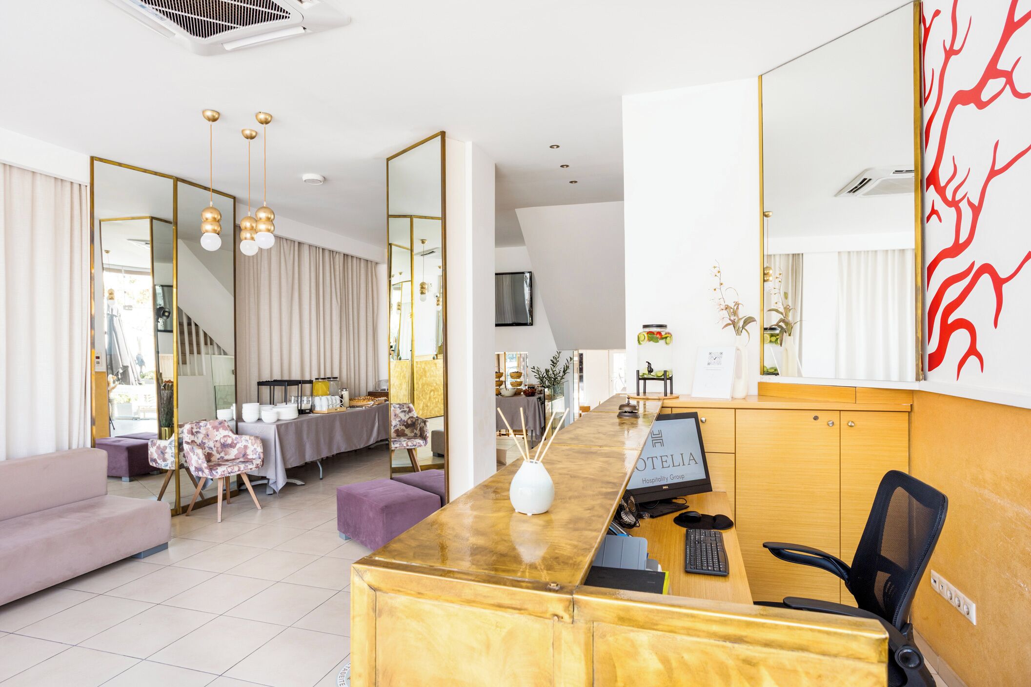 Un espace d’accueil d’hôtel comprenant un comptoir en marbre, un grand miroir, un canapé et un coin repas.