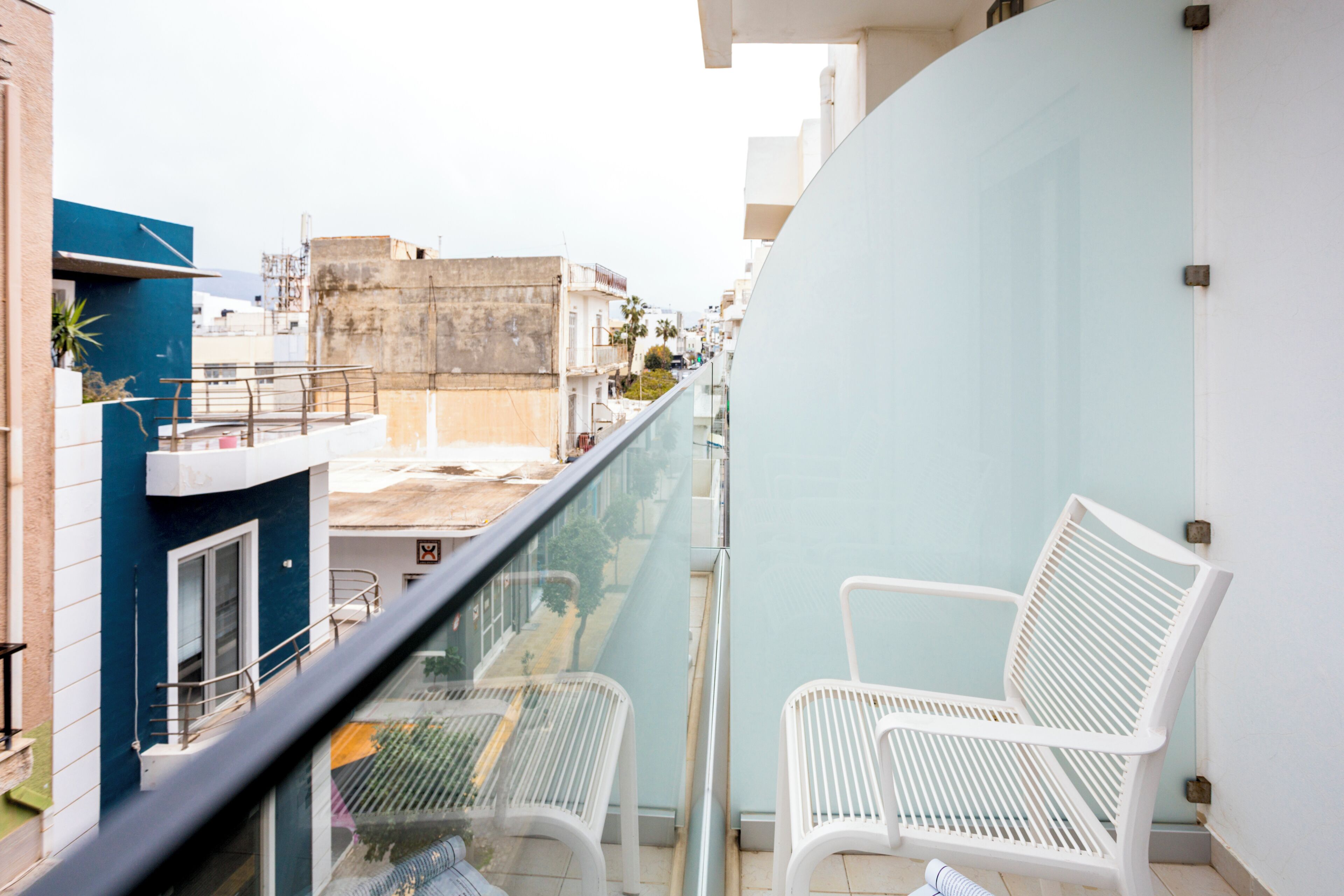 A balcony with two white chairs, a glass railing, and a view of buildings.