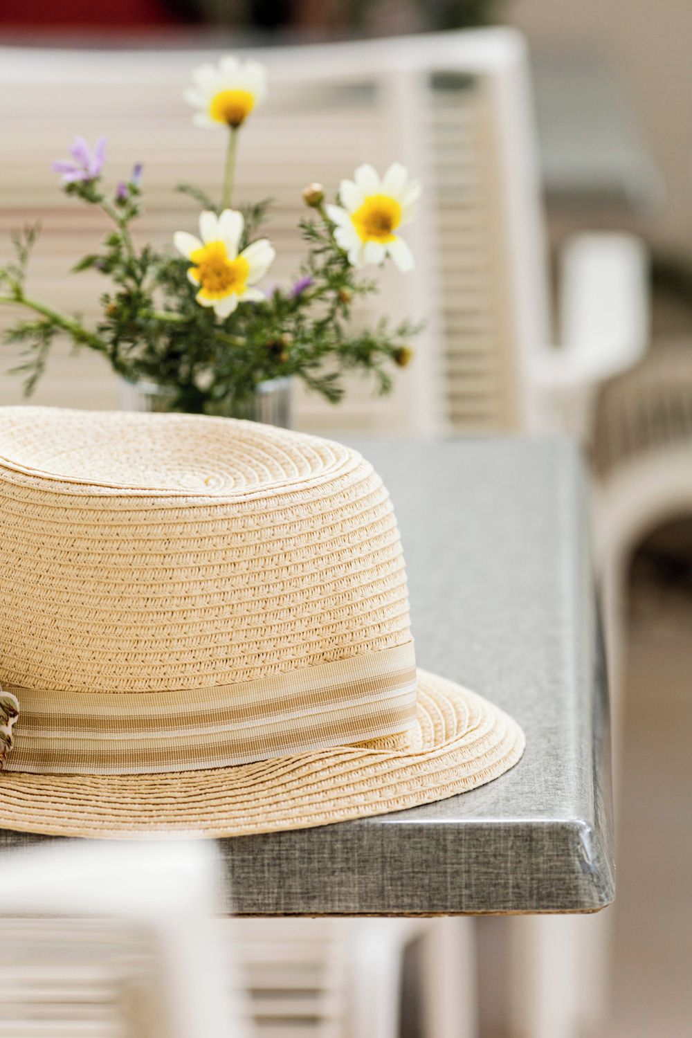 A woven straw hat on a wooden table with a vase of flowers.