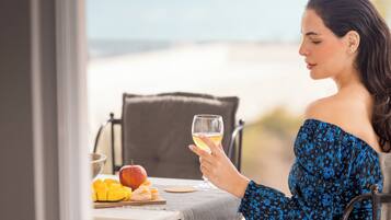 Una persona sentada a una mesa con una copa de vino, una manzana y fruta cortada, con vista a una playa.