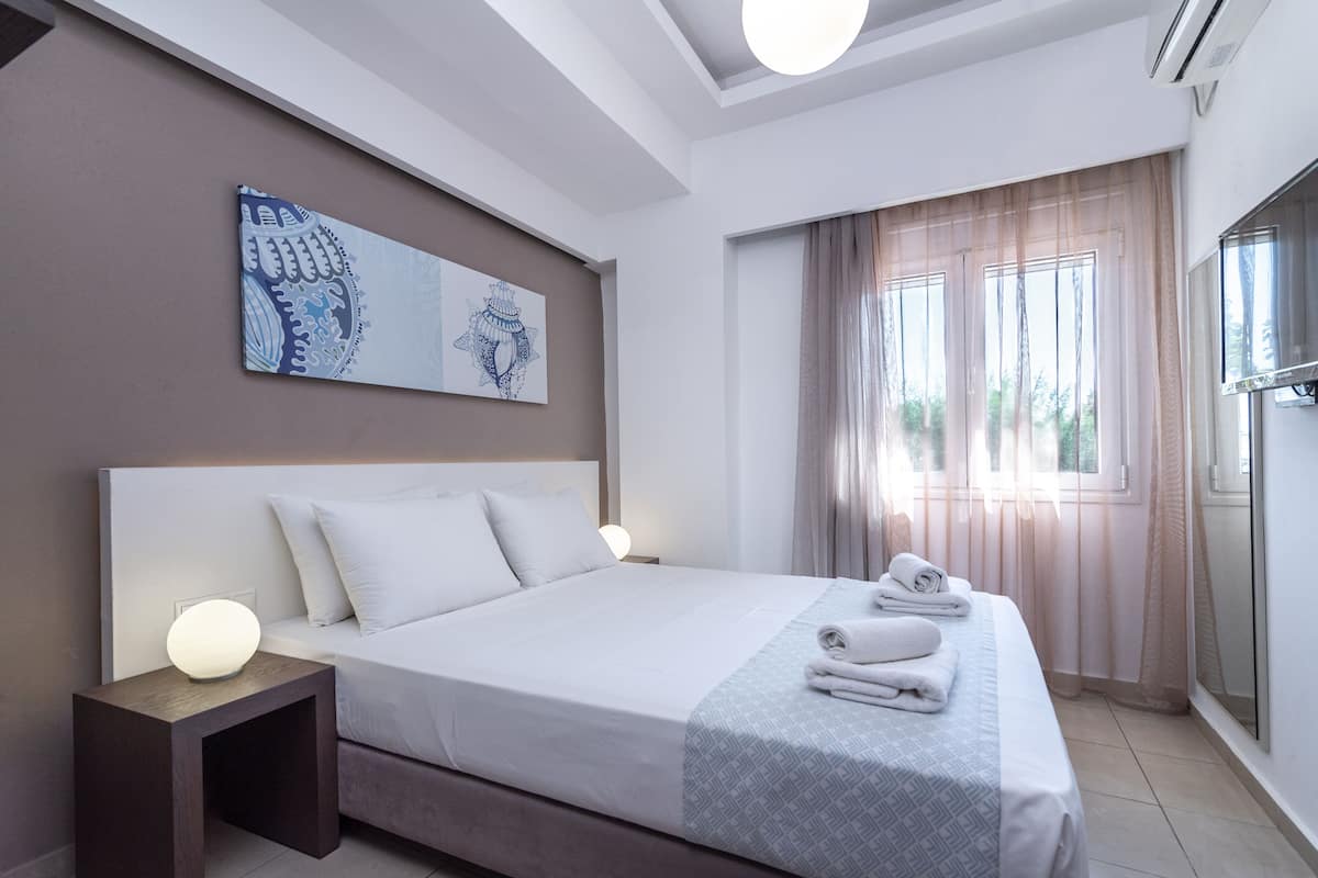 A modern hotel room with a large bed, bedside lamps, a wall-mounted artwork, and a window with sheer curtains.