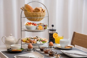 A breakfast setting with a three-tiered stand, a teapot, cups, a glass of orange juice, and various breakfast items. - Coral Apts - Hotelia Hospitality Group (Ierapetra)