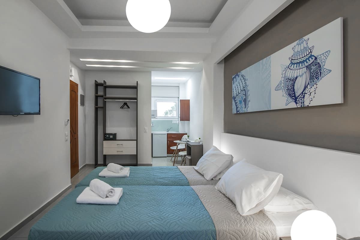 A hotel room with two beds, a TV, a painting, and a kitchenette in the background.