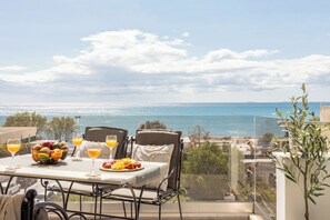 A balcony with a table set for breakfast, a view of the sea, and a clear sky. - Coral Apts - Hotelia Hospitality Group (Ierapetra)
