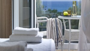 Un balcone con una sedia in vimini, un tavolino con un bicchiere, una mela gialla e una bottiglia.