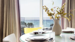 Un tavolo da pranzo con piatti, posate e un vaso di fiori, con vista sul mare attraverso una finestra.