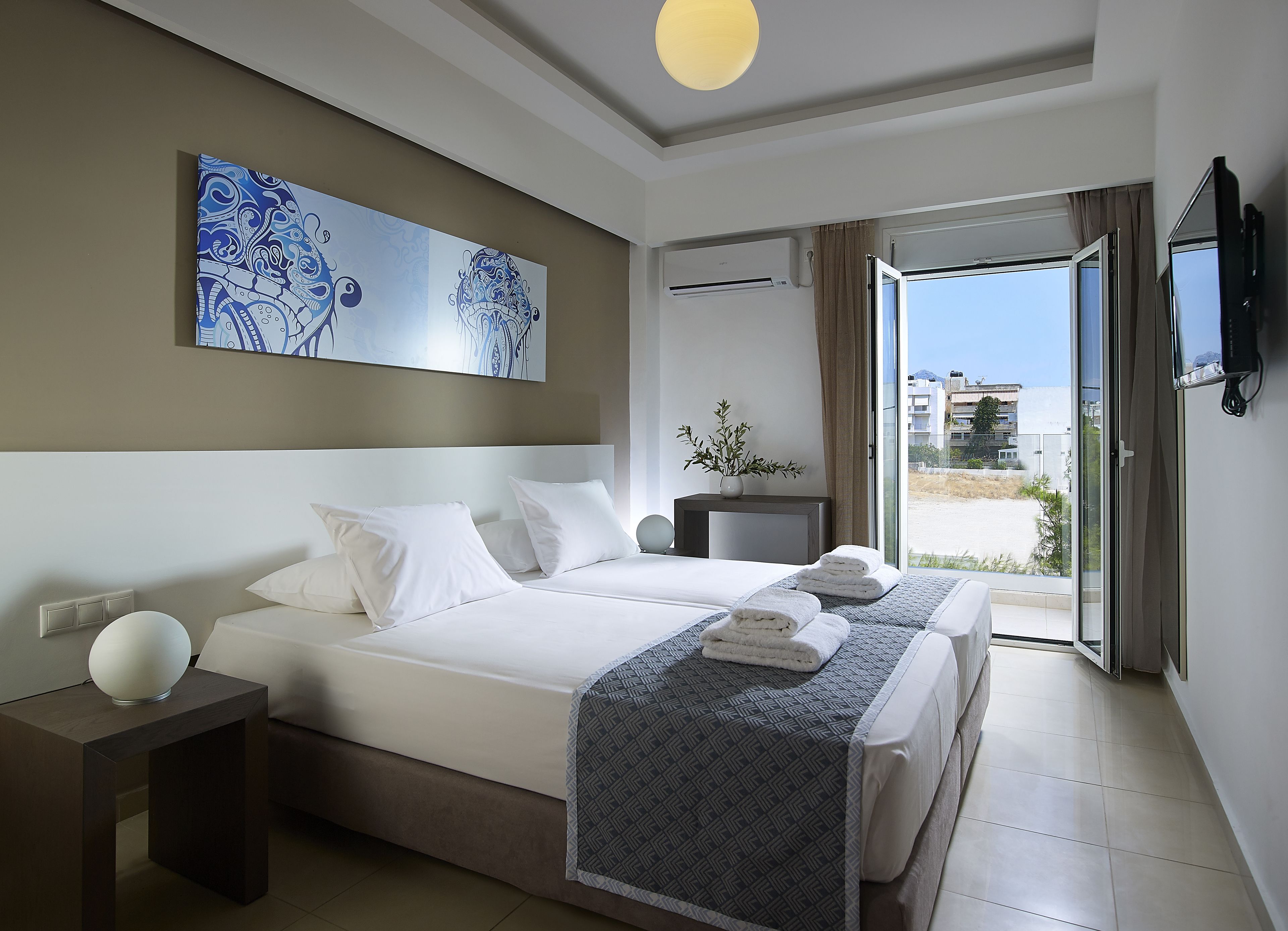 Une chambre d’hôtel avec un grand lit, une table de chevet, une petite table avec un vase, un téléviseur fixé au mur et une vue sur l’extérieur.