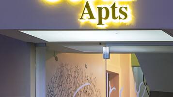 L’entrée d’un immeuble, avec une enseigne indiquant « Coral Apts » et une porte décorative en verre ornée d’un motif représentant un arbre.