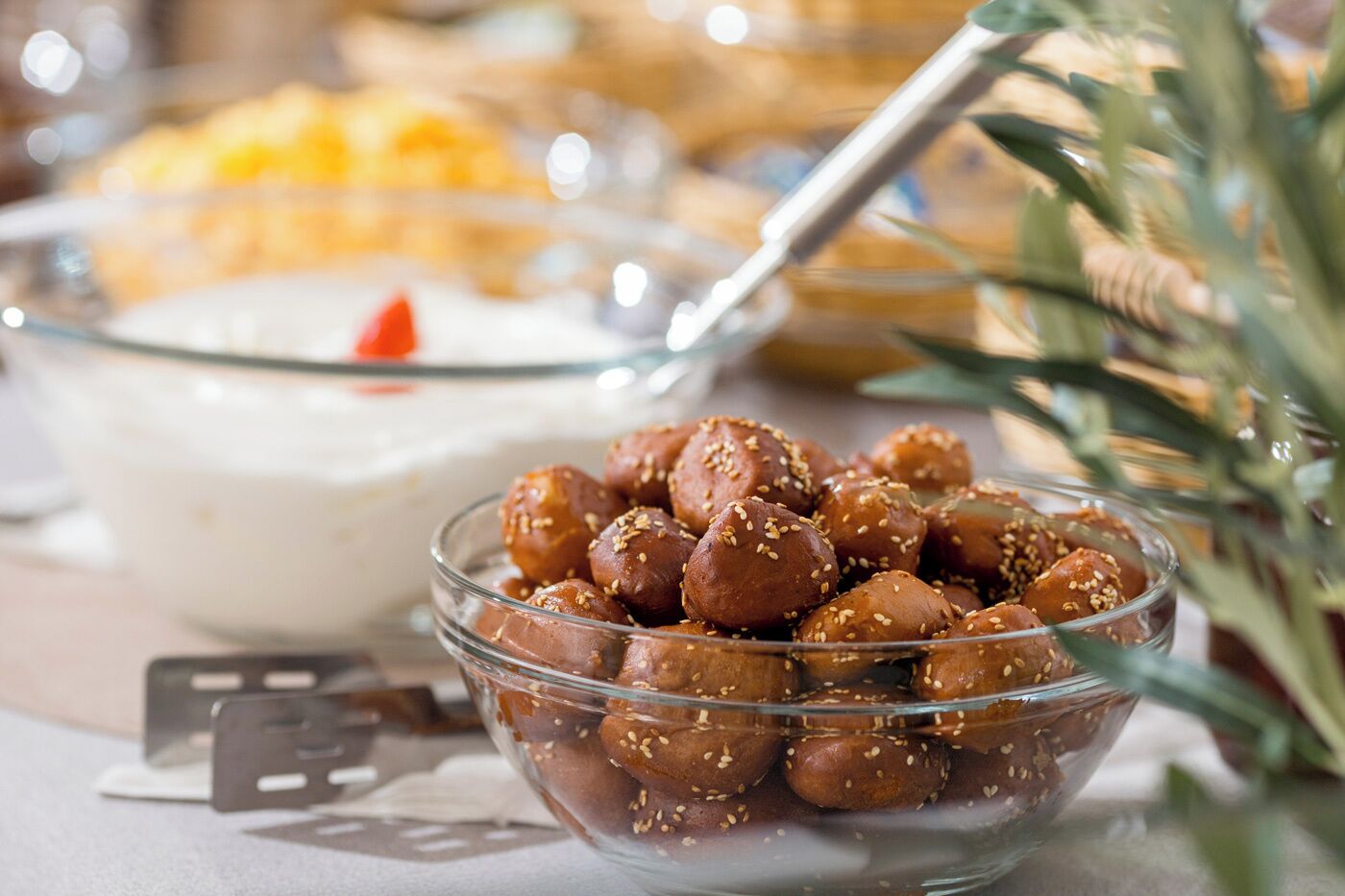 A glass bowl filled with sesame seed-covered sweets, a candle, and a blurred background with a plant.