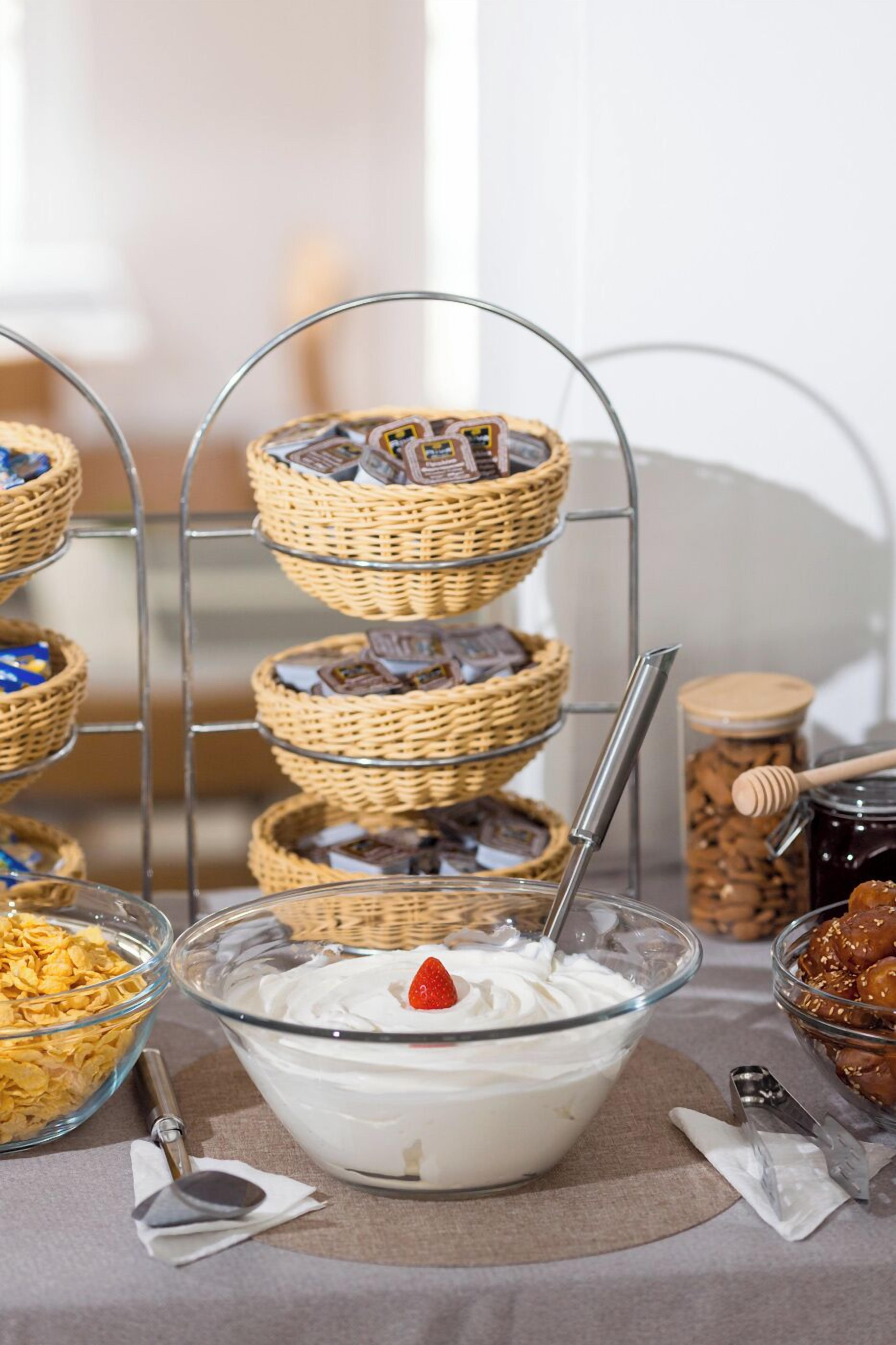 A buffet setup with a bowl of yogurt parfait, a tiered wicker basket with chocolates, and a jar of honey.