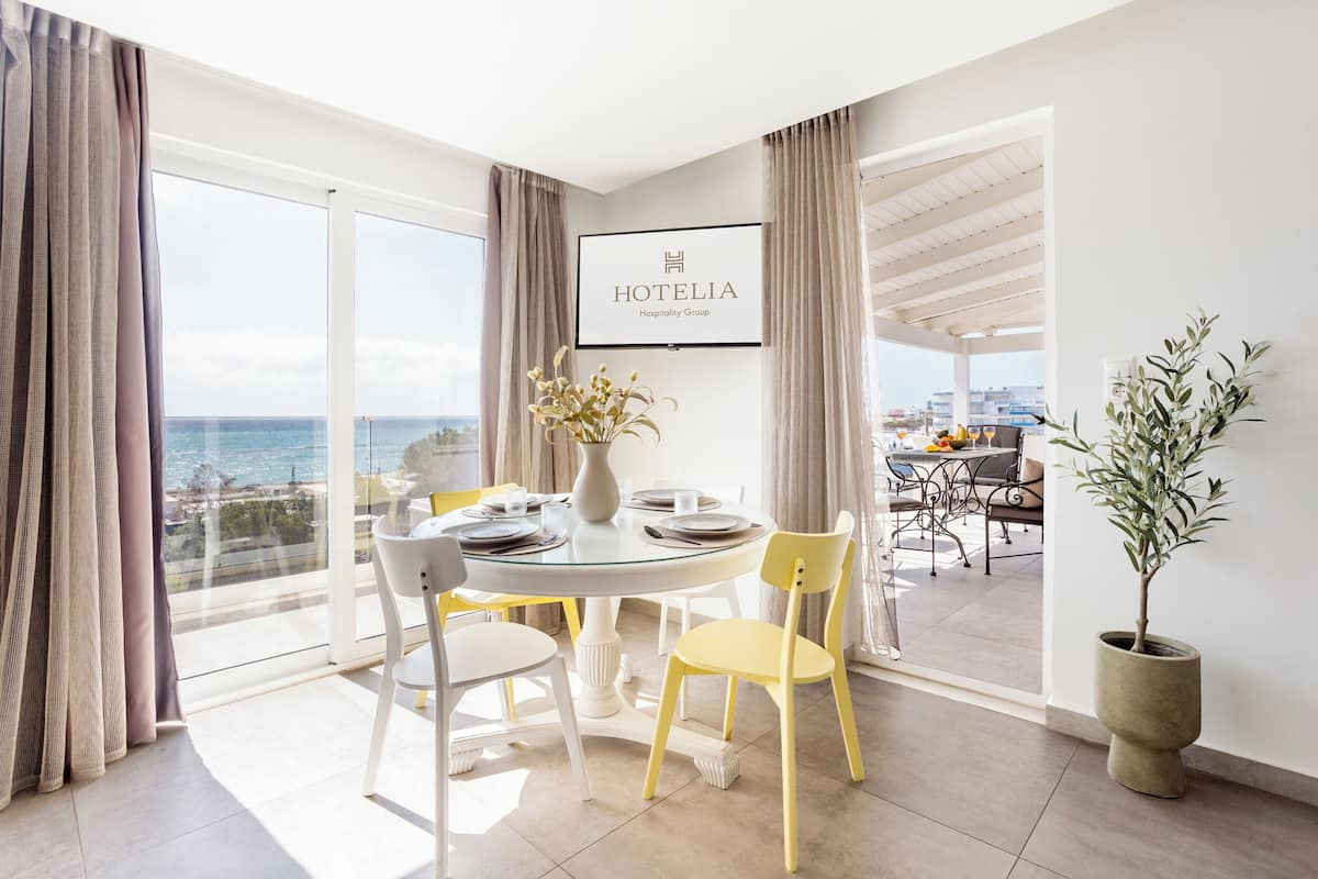 A hotel room with a balcony, a dining table set for four, and a view of the sea.