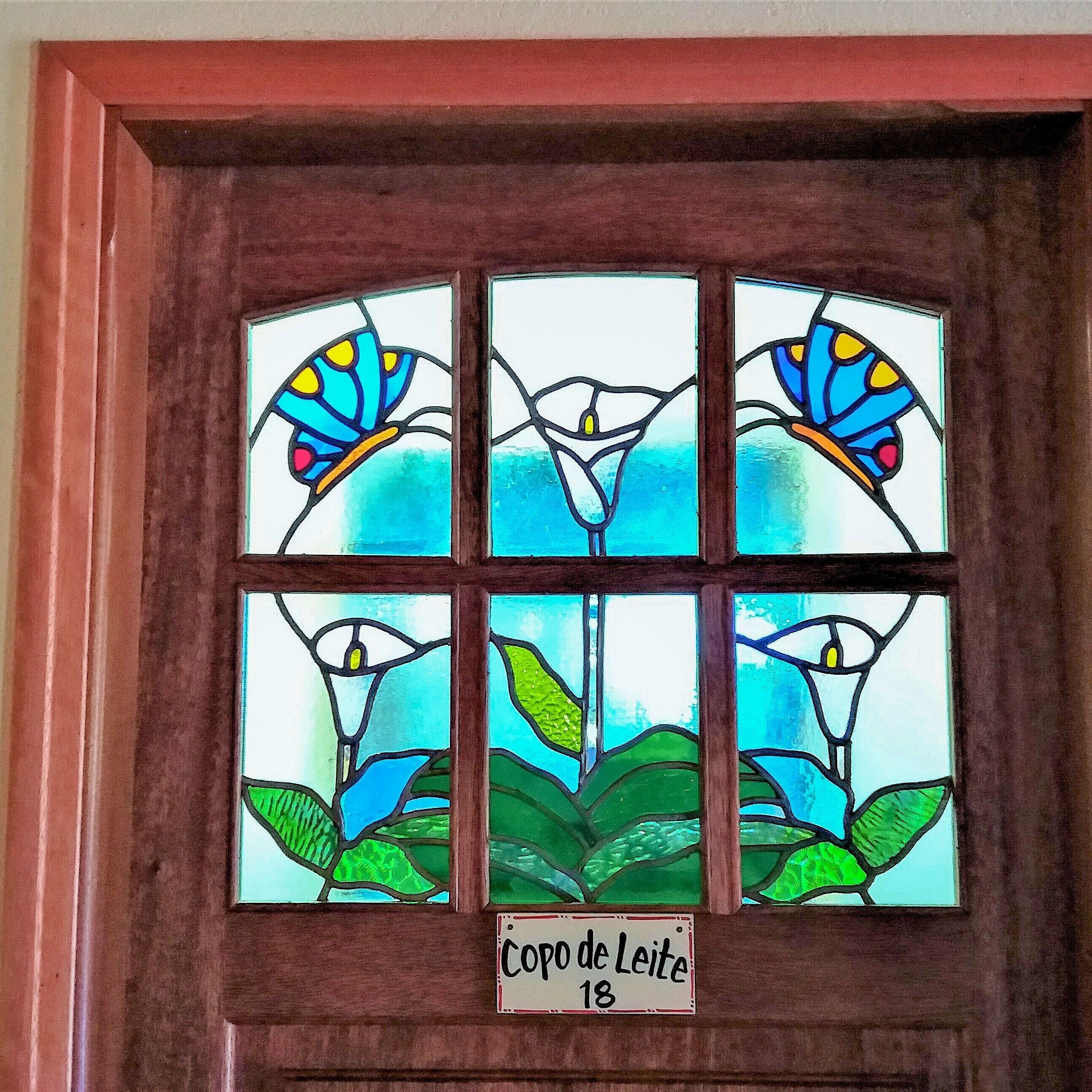 Ein Buntglasfenster mit floralen und Schmetterlingsmotiven, beschriftet mit "Coro de Leite 18".