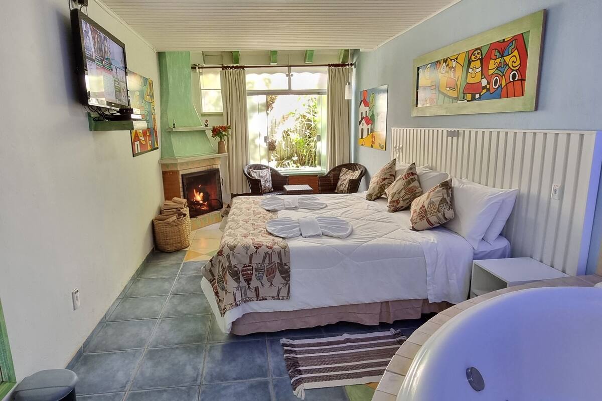 A bedroom with a large bed, a sitting area with a fireplace, and a bathtub.