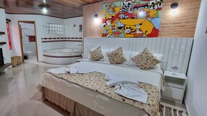 Un dormitorio moderno con una cama grande, una mesita pequeña y una silla. Hay un cuadro abstracto y colorido en la pared y una chimenea con azulejos.