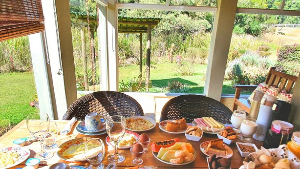 Una mesa de desayuno al aire libre con diferentes platos, vasos y una silla de mimbre.