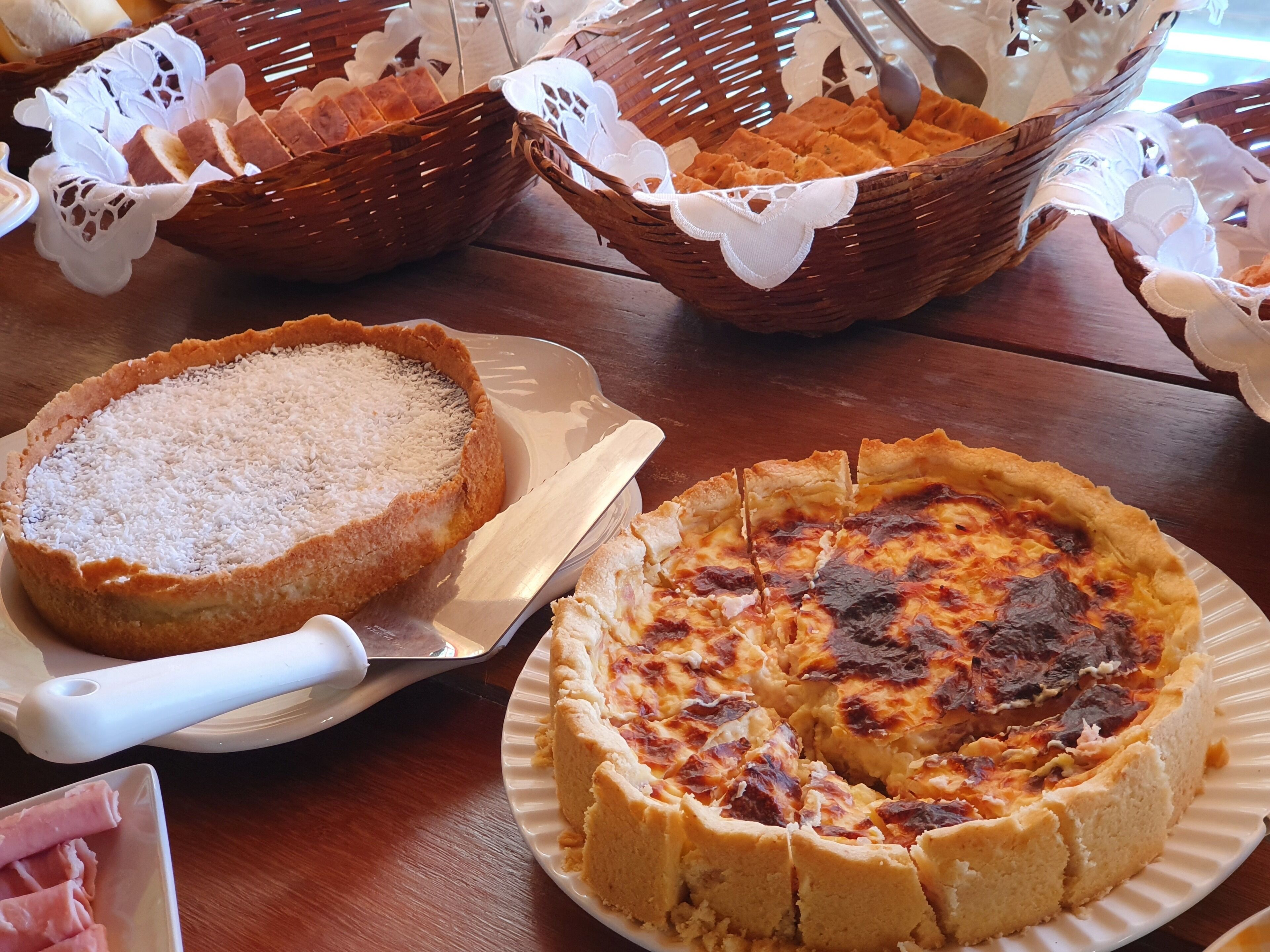 Une table avec deux tartes, l’une recouverte de noix de coco et l’autre avec une croûte légèrement brûlée, et une assiette de viande tranchée.