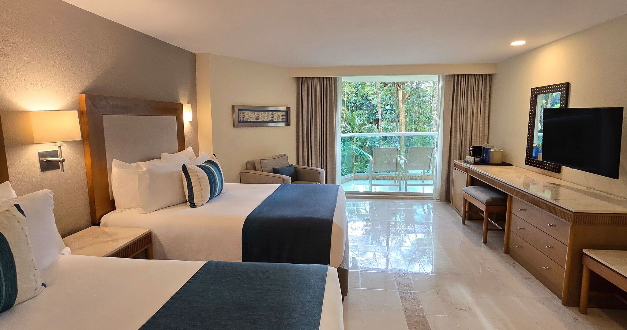 Habitación de hotel con dos camas, un escritorio, un televisor y un balcón con vistas.