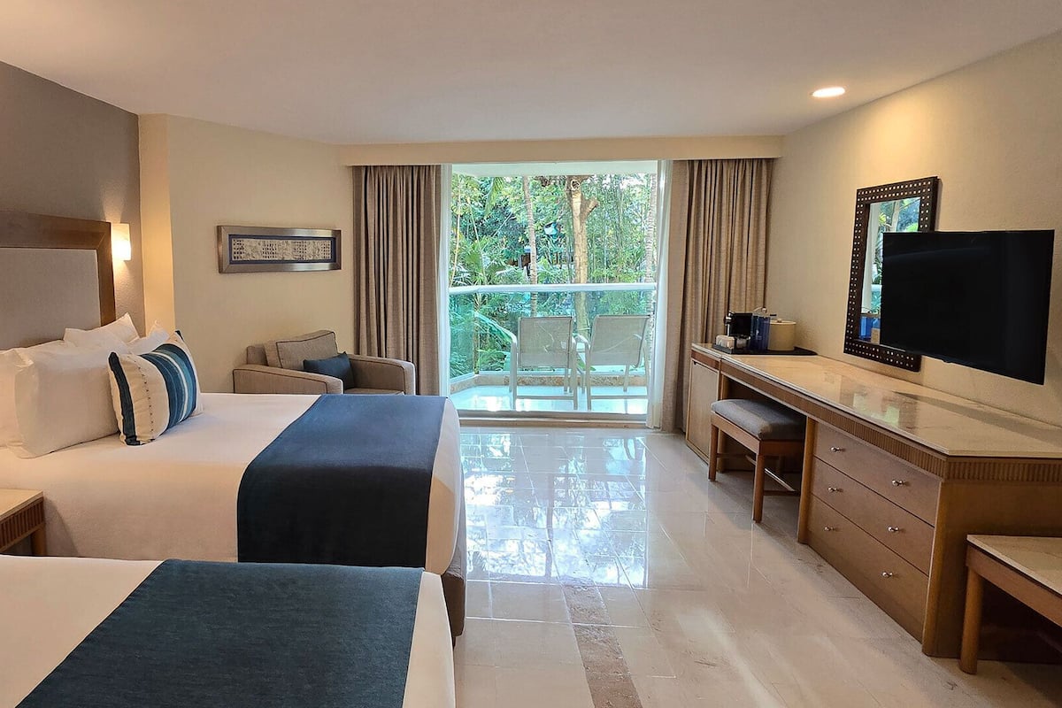 Habitación de hotel con dos camas, un escritorio, un televisor y un balcón con vistas.