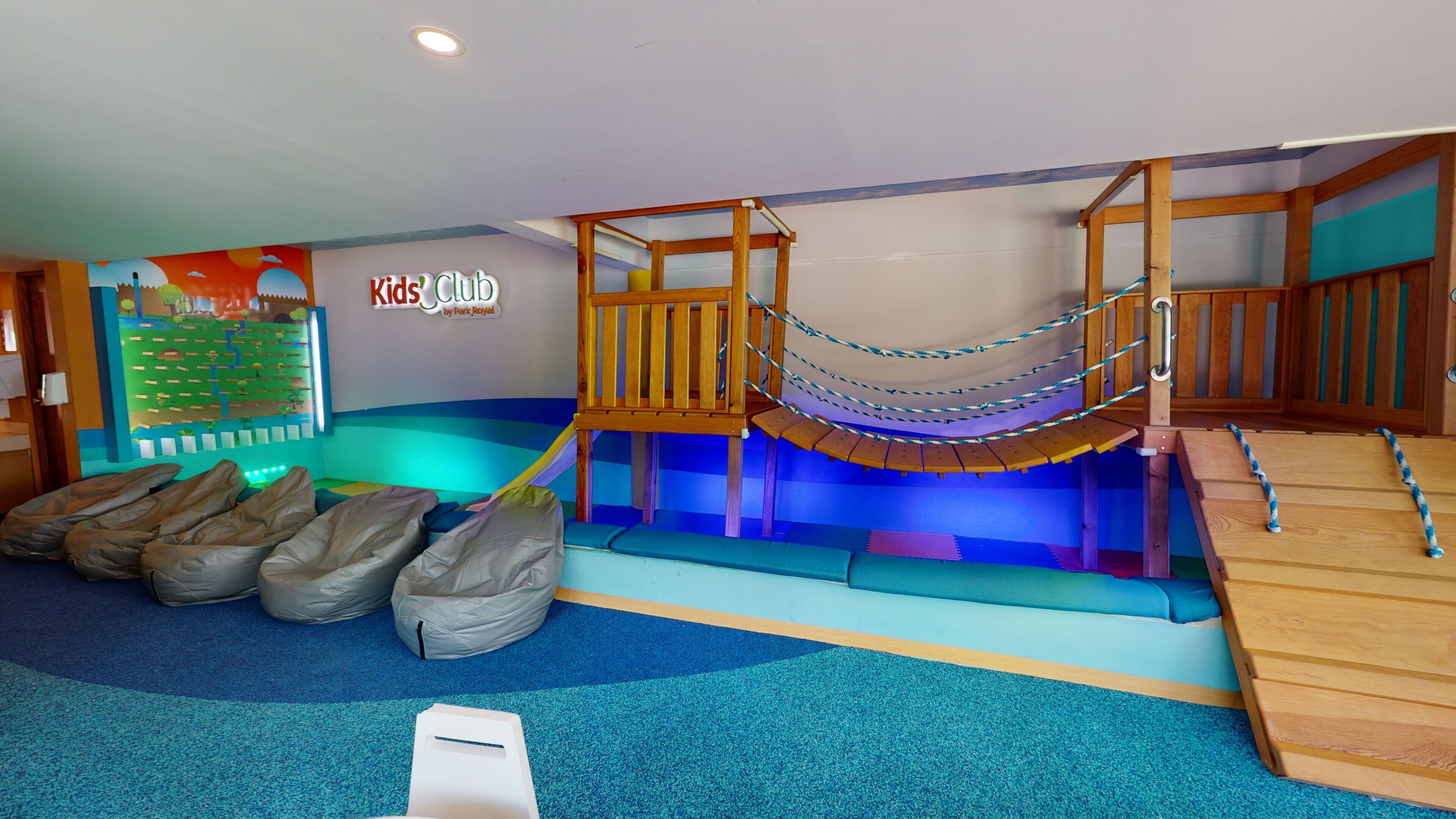 A children's play area with a climbing structure, padded seating, and a wall with a colorful mural.
