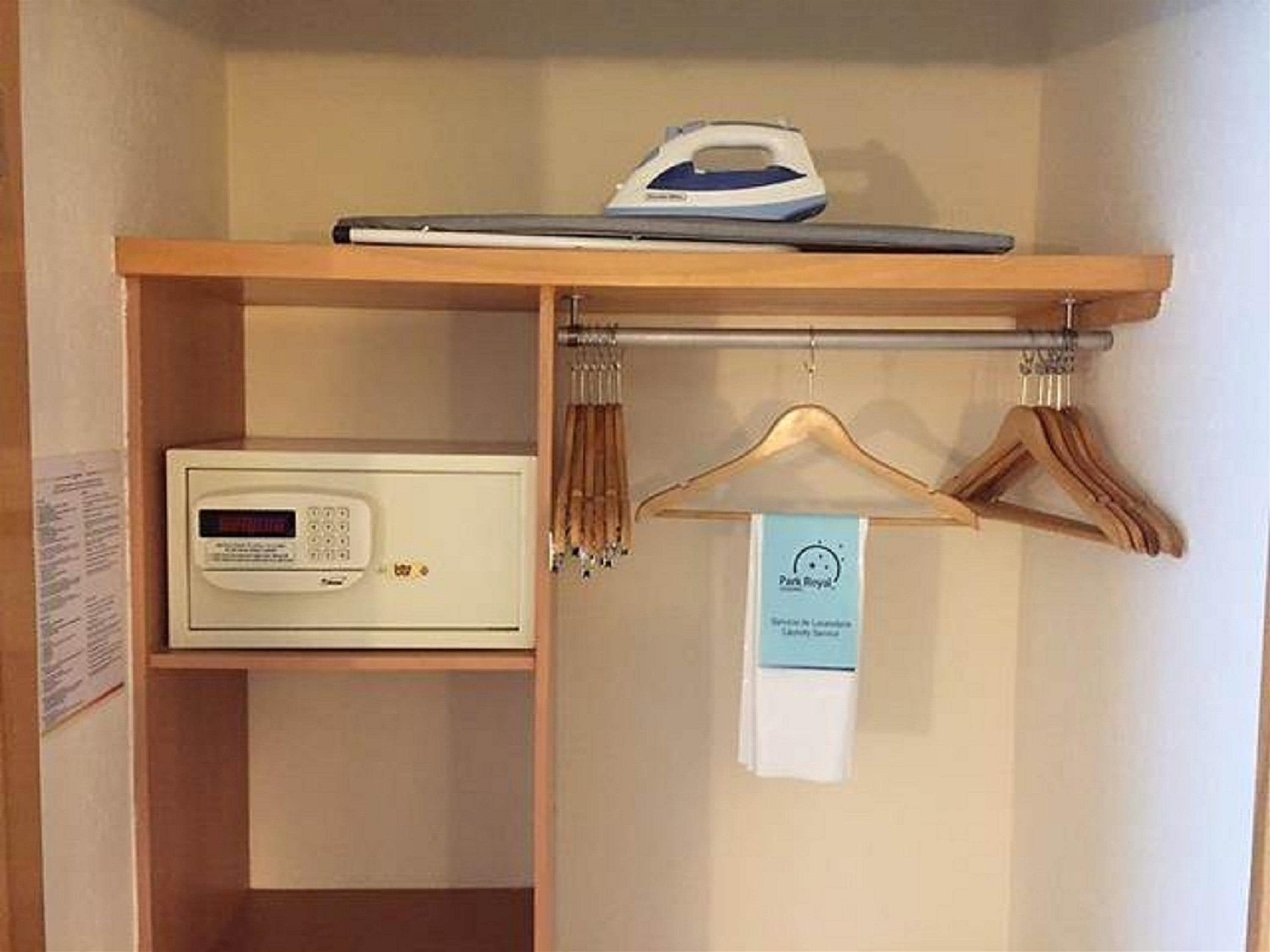 A hotel room with a wooden shelf holding an iron and a microwave. There is a wooden hanger rack with a tag hanging from it.
