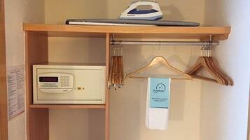 A hotel room with a wooden shelf holding an iron and a microwave. There is a wooden hanger rack with a tag hanging from it.