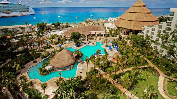 A resort with a large pool, a thatched-roof structure, and a view of the ocean. - Grand Park Royal Cozumel - All Inclusive (Cozumel)