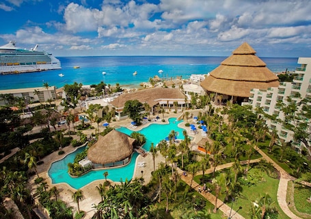 A resort with a large pool, a thatched-roof structure, and a view of the ocean.