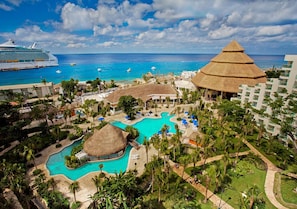 A resort with a large pool, a thatched-roof structure, and a view of the ocean.