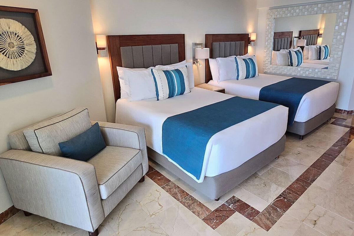 A hotel room with two beds, a sofa, and a large mirror.