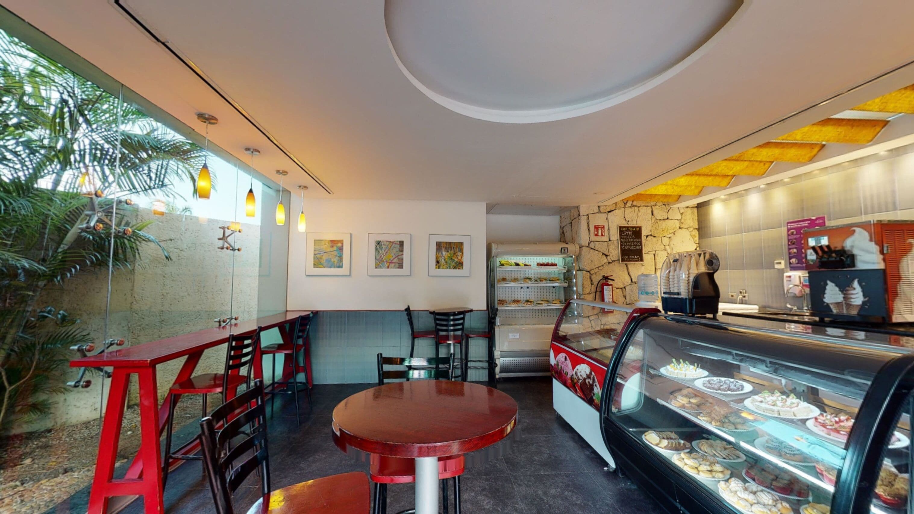 Cafetería interior con un expositor de postres, mesas y sillas de madera, y un panel de menú colgado en la pared.
