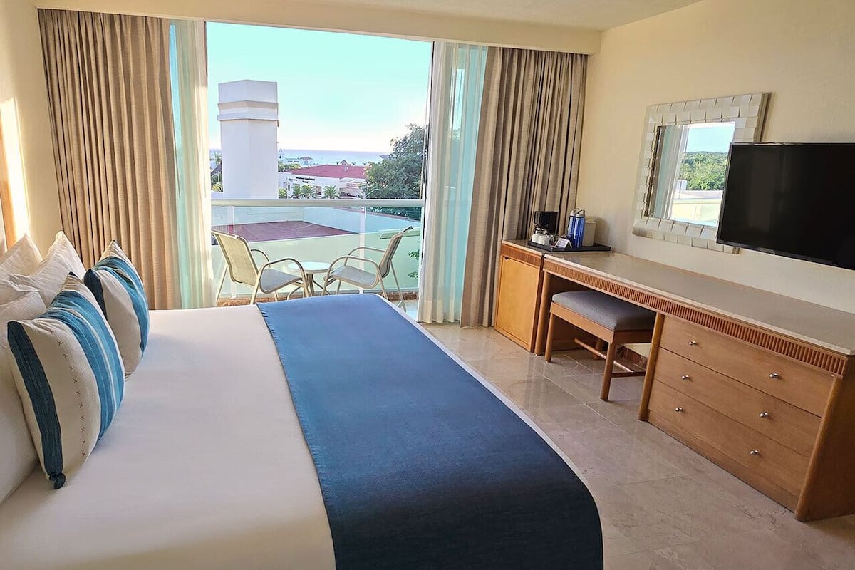 A hotel room with a large bed, a desk, a chair, a television, and a view of the outdoors.