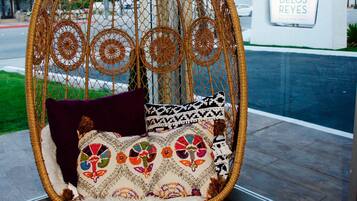 A wicker hanging chair with colorful cushions and a fluffy white throw inside a room with a large window.