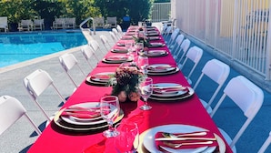 A dining table set for a meal with chairs on both sides, overlooking a pool and palm trees. - Delos Reyes Palm Springs (Palm Springs)