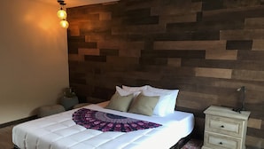 A neatly made bed with a patterned throw, a bedside table with drawers, a nightstand, a wall-mounted light fixture, and a patterned rug. - Delos Reyes Palm Springs (Palm Springs)