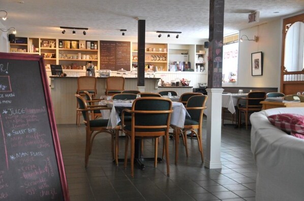 Un interior de restaurante con sillas y mesas de madera, un menú en pizarra y una zona de mostrador.
