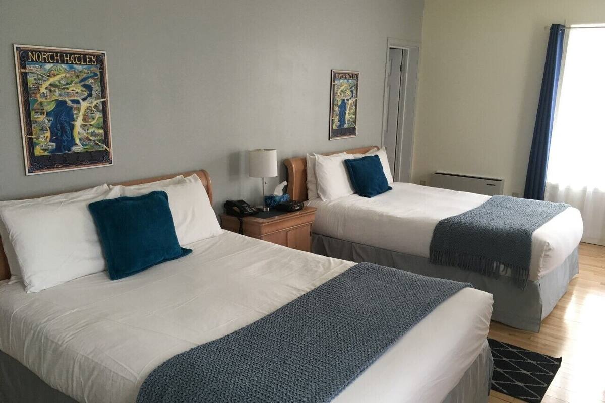 Habitación de hotel con dos camas, una mesita de noche, una lámpara y dos carteles en la pared.