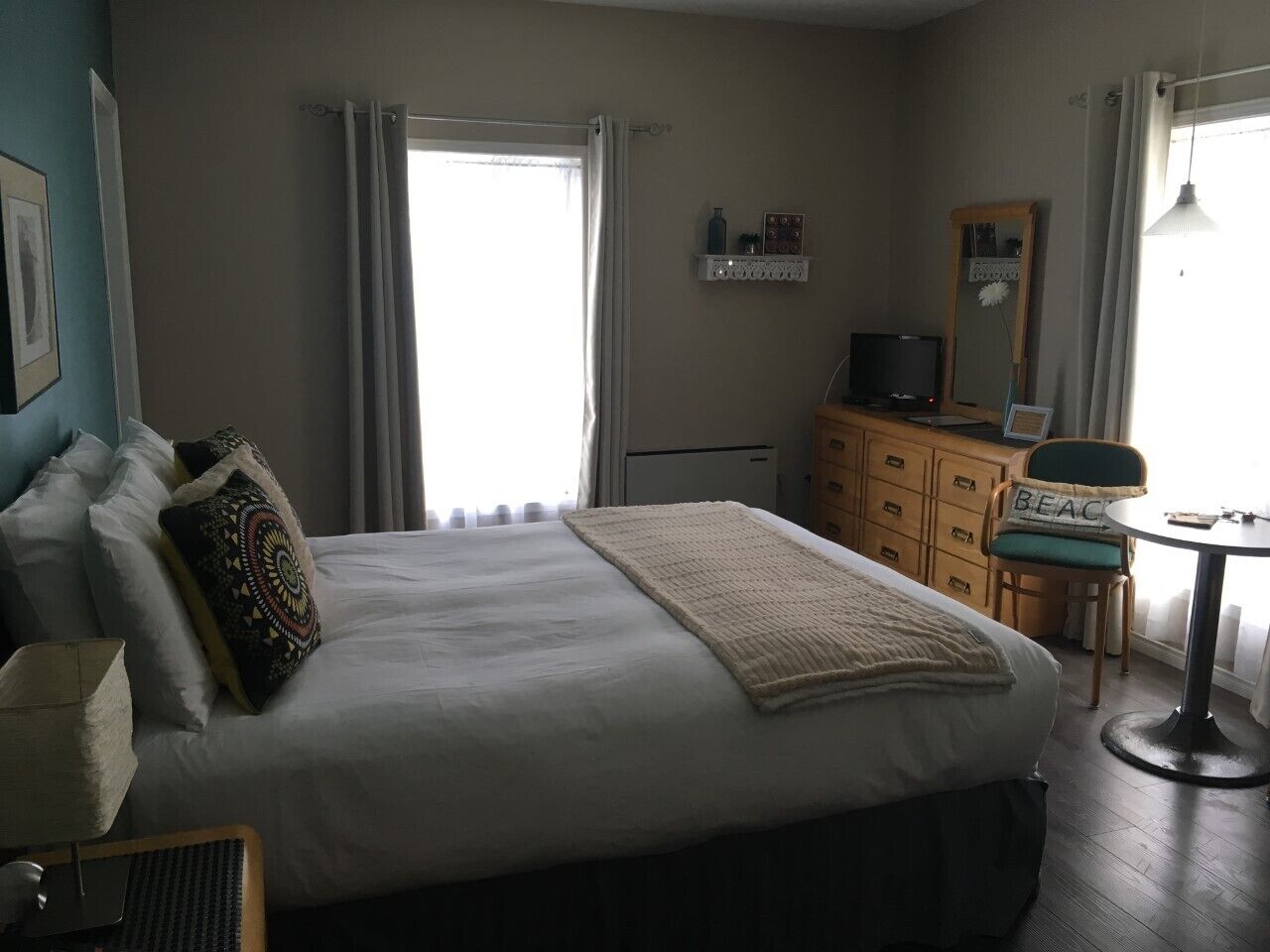 A bedroom with a large bed, a desk, a chair, a dresser, and a window with curtains.