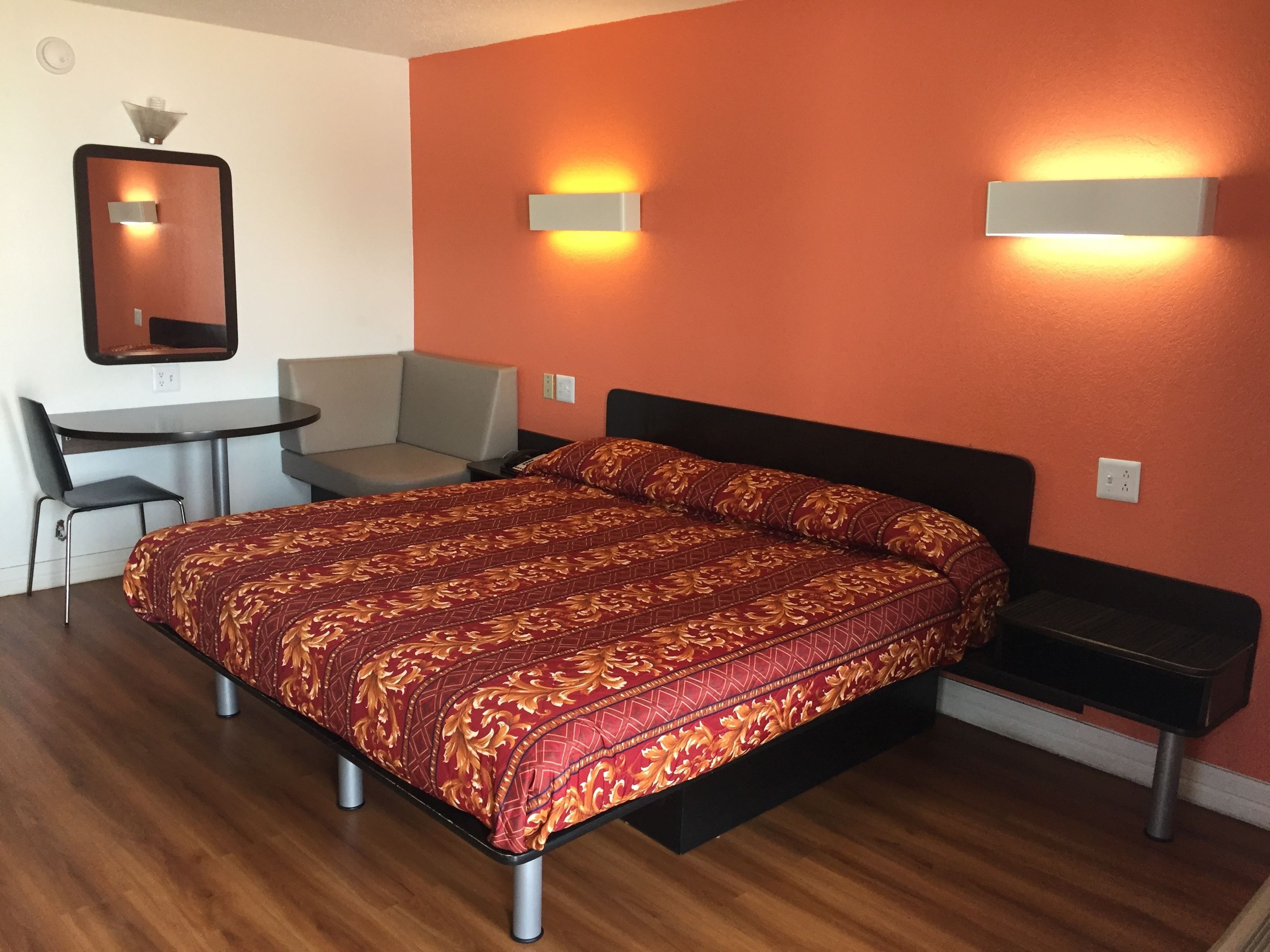 A hotel room with a bed, a desk, a chair, and two wall-mounted lights.