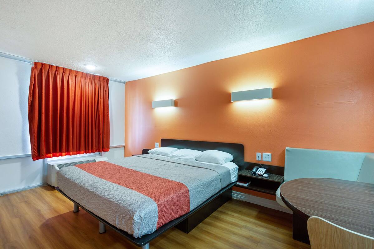 A hotel room with a bed, bedside table, and a small round table.