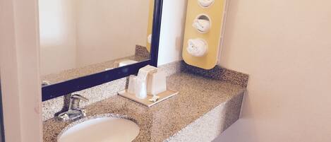 A bathroom with a granite countertop, a white sink, a mirror, and a towel dispenser.