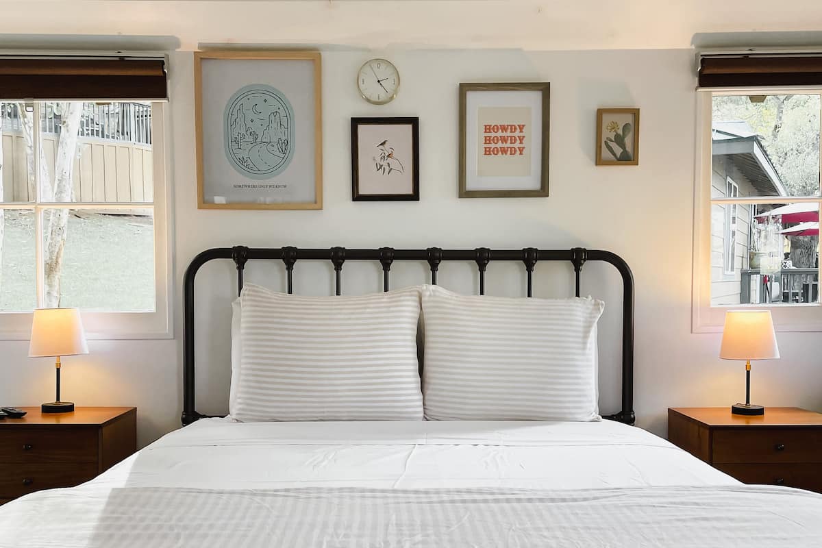 A neatly made bed with a metal headboard, two bedside tables with lamps, and framed artwork on the wall.
