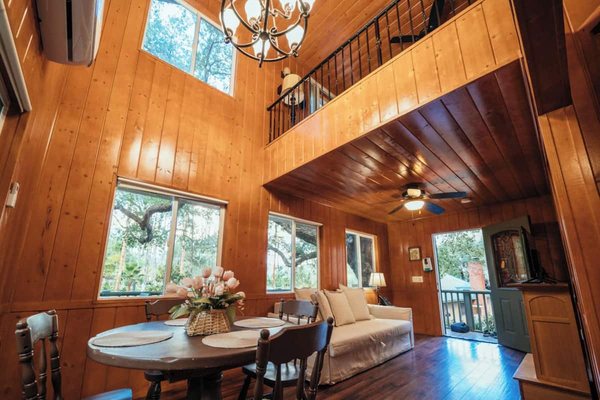 A wooden cabin interior with a dining area, a sofa, and a balcony.