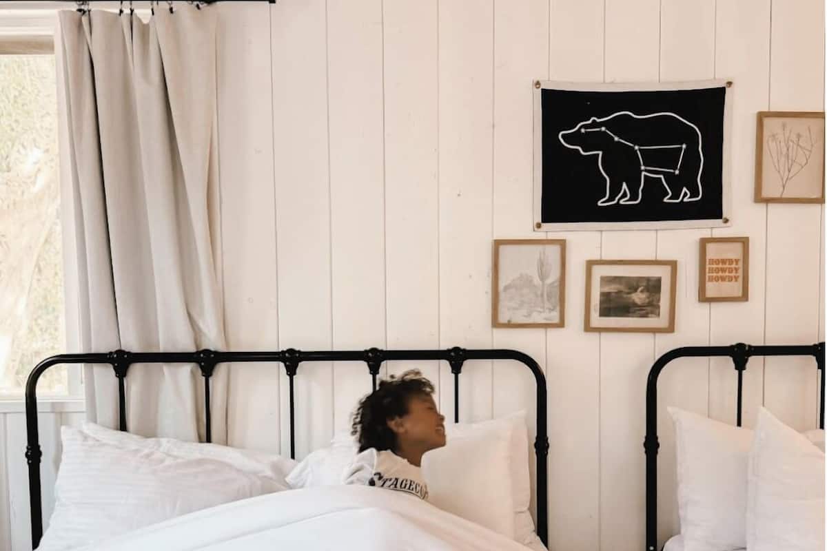 A bedroom with two beds, white bedding, a black bear silhouette artwork, and framed pictures on the wall.