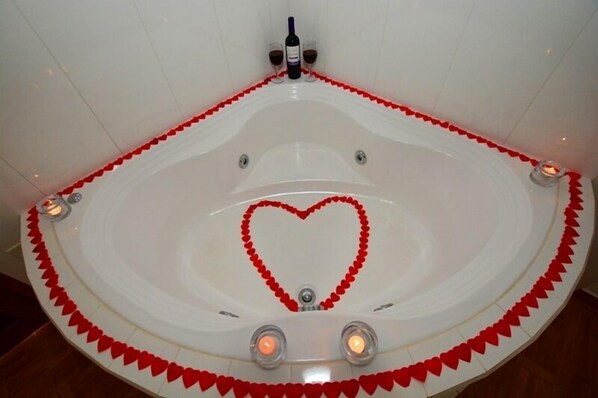 Un jacuzzi circular con una disposición en forma de corazón de pétalos de rosa roja, rodeado de velas.